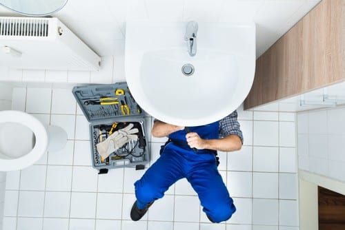 Plombier Amboise - homme qui règle la tuyauterie d'un lavabo